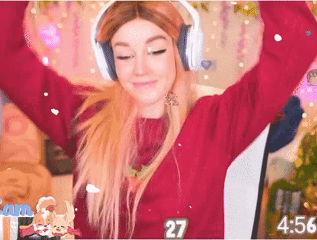 a woman wearing headphones and a red sweater is dancing in front of a computer screen with the time of 4:56
