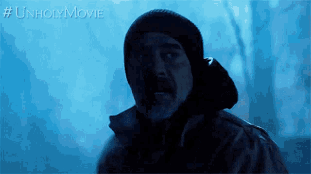 a man in a black hat is standing in a dark forest with #unholymovie written below him