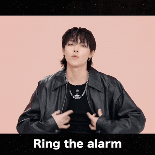 a man wearing a black jacket and a necklace says " ring the alarm " in a pink background