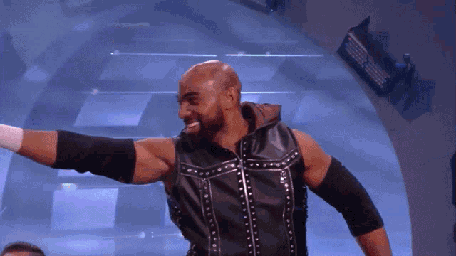 a wrestler in a black vest with studs on it is smiling