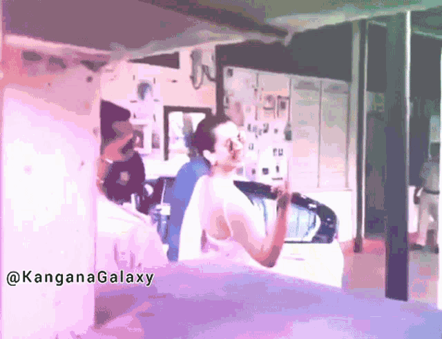 a woman in a white dress is standing in front of a car and a sign that says kanganagalaxy on it
