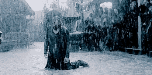 a man is kneeling in the rain with a crowd watching .