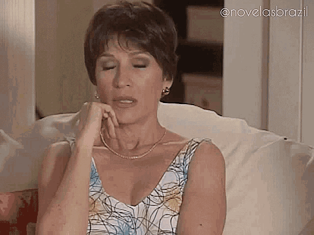 a woman is sitting on a couch with her hand on her chin and looking at the camera .