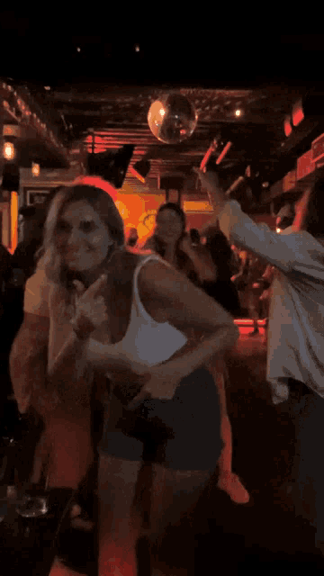 a woman in a white tank top is dancing in a crowded bar