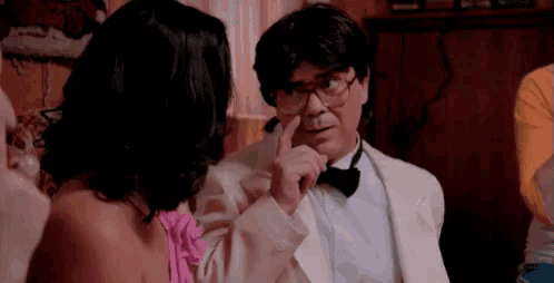 a man in a tuxedo and bow tie is pointing at a woman .