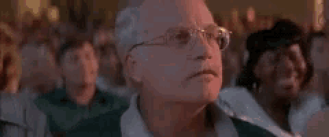 an older man wearing glasses is sitting in a crowd of people watching a concert .