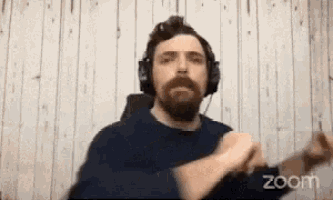 a man with a beard wearing headphones is on a zoom call with his hands in the air
