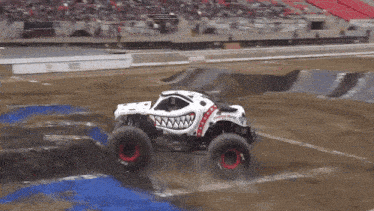a monster truck with a shark face on the side is driving on a dirt track