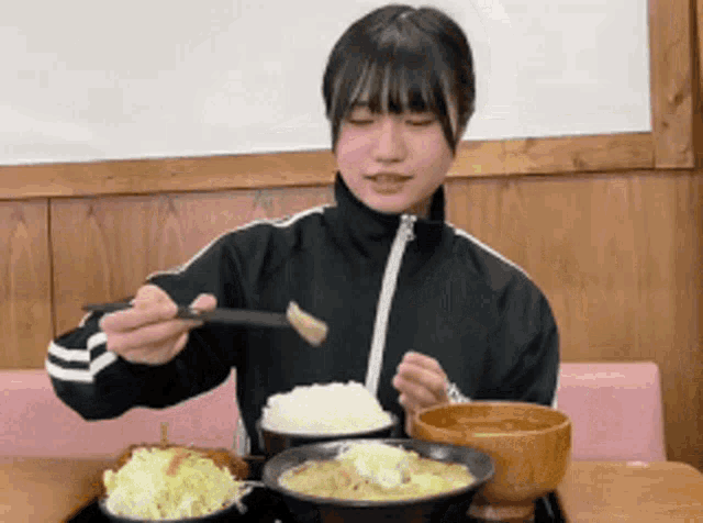 a girl in a black jacket is sitting at a table eating food