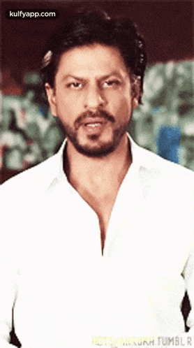 a man with a beard is wearing a white shirt and looking at the camera .