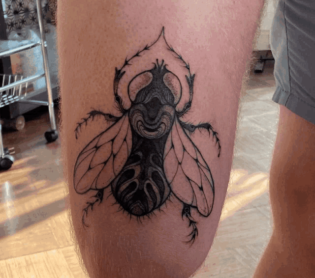 a black and white tattoo of a beetle on a person 's leg