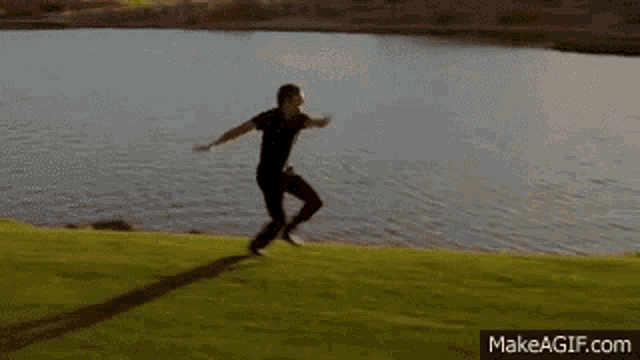 a man is jumping in the air on a grassy field near a lake .