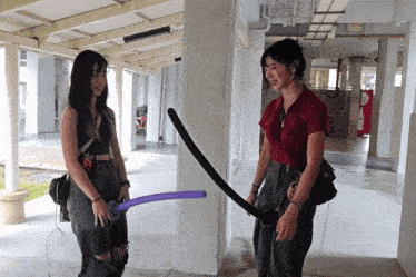two women are playing with balloons in a hallway and one of them is holding a purple balloon