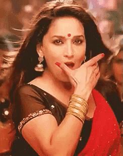 a woman wearing a black top and a red saree is making a funny face with her hand .