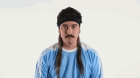a man with long hair and a mustache is wearing a blue shirt and headband .