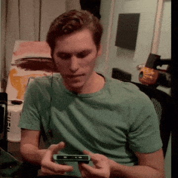 a man in a green shirt is holding a cell phone in his hands