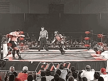 two men are wrestling in a wrestling ring with a referee in the background .