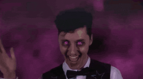 a man in a tuxedo with purple eyes and a bow tie is making a funny face .