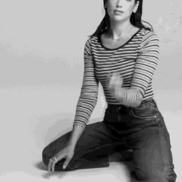 a black and white photo of a woman wearing a striped shirt and jeans kneeling on the floor .