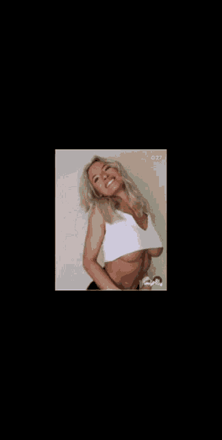 a woman in a white crop top is smiling and looking at the camera while standing in front of a wall .