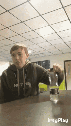 a boy wearing a north face sweatshirt sits at a table with a bottle of water