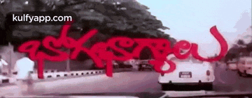 a white car is driving down a street with red writing on the side of the road .