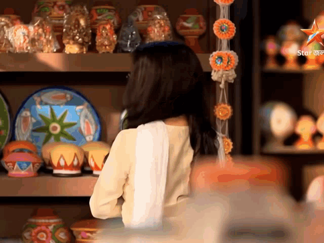 a woman in a white dress stands in front of a shelf full of plates