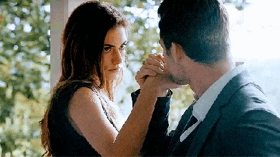 a man and a woman are holding hands and looking at each other . the woman is wearing a black dress .