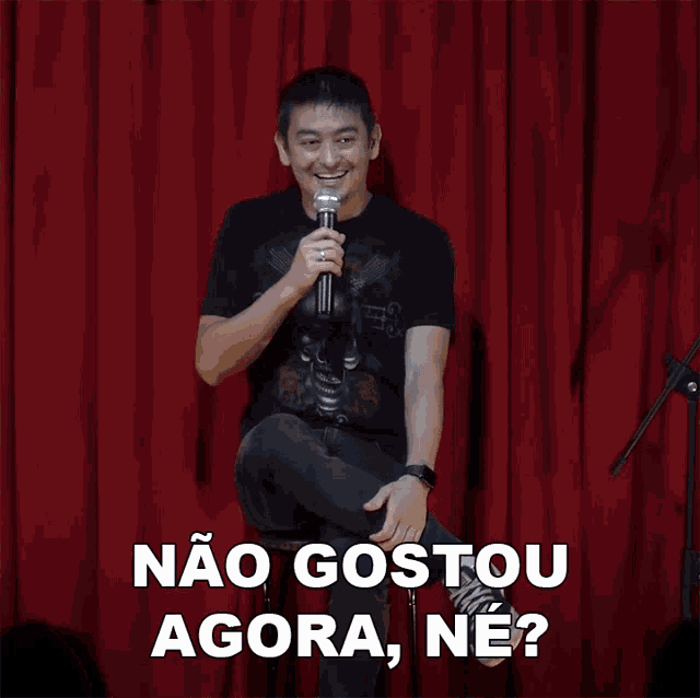 a man is holding a microphone in front of a red curtain and says não gostou agora ne ?