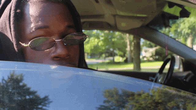 a man wearing sunglasses and a black hoodie looks out the window of a car
