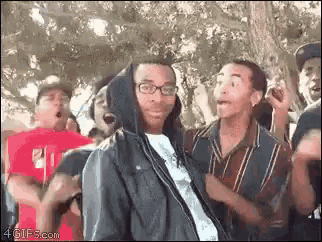 a group of people are dancing in a park and one of them is wearing a hooded jacket .