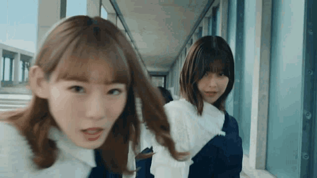 two girls are walking down a hallway and one of them is looking at the camera .