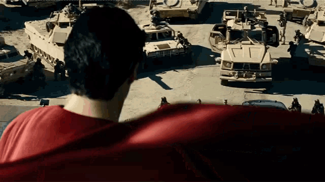 a man in a red cape stands in front of a row of military vehicles
