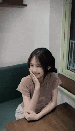 a young girl sits at a table with her hand on her face