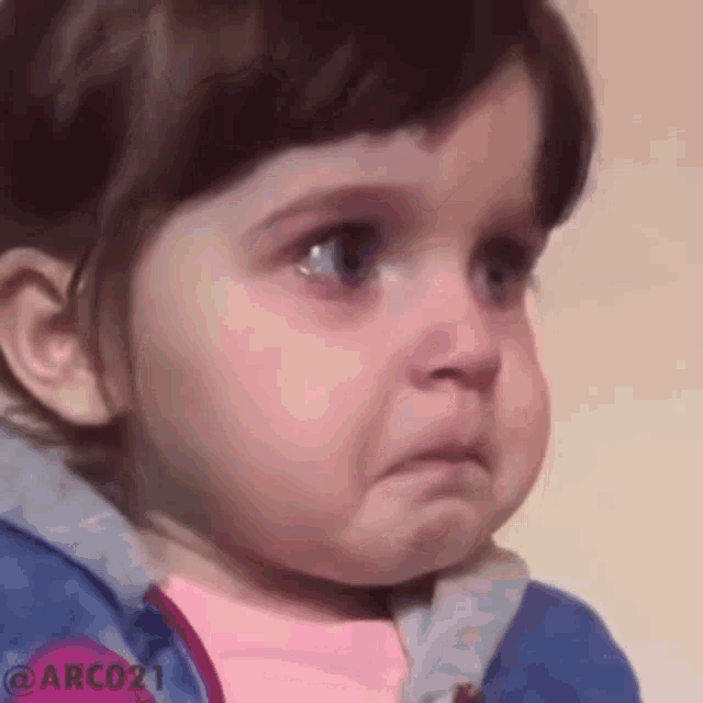 a baby girl is crying and making a funny face while wearing a blue jacket .