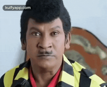 a close up of a man with a mustache wearing a yellow and black jacket and a red shirt .
