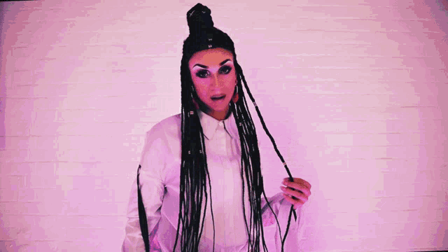 a woman with dreadlocks is standing in front of a pink wall with a rainbow colored background .