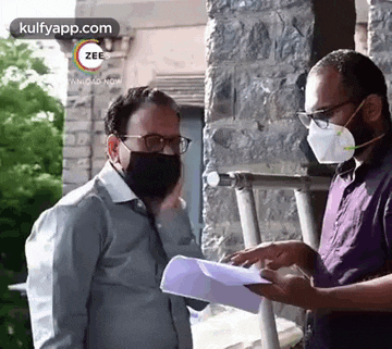 two men wearing face masks are standing next to each other and talking .