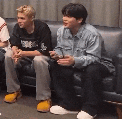 two men are sitting on a couch with their legs crossed and talking to each other .