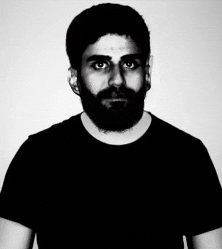 a man with a beard wearing a black shirt is looking at the camera .