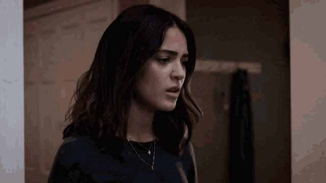 a woman wearing a black shirt and a necklace is standing in a room