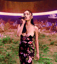 a woman in a floral dress is singing into a microphone in a field