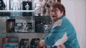 a man in a blue jacket is standing in front of a shelf filled with toys .