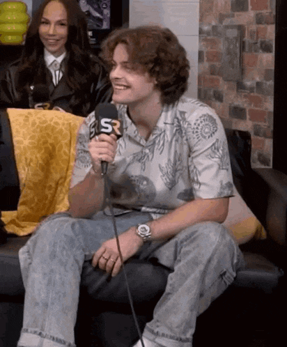 a young man is sitting on a couch holding a microphone and smiling .
