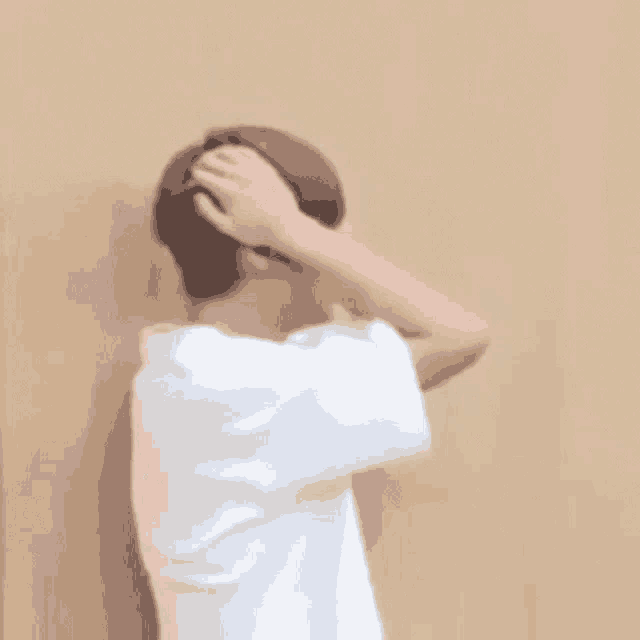 a man in a white shirt is standing in front of a wooden wall and holding his hair .