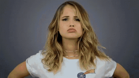 a woman in a white t-shirt is making a funny face while standing with her hands on her hips .
