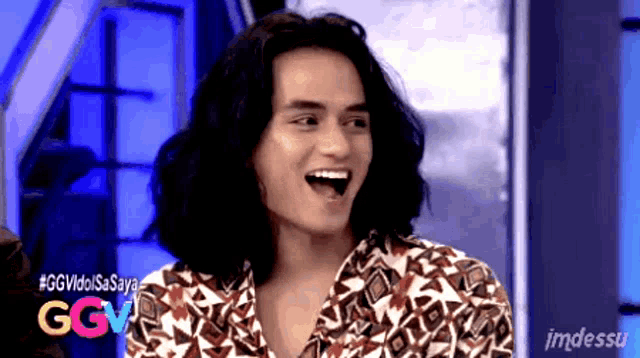 a man with long hair is laughing in front of a sign that says ggvidisasaya