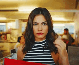 a woman wearing a black and white striped top holds a red bag