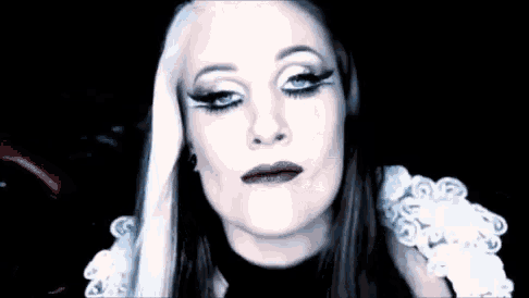 a woman with long white hair and red lips is wearing a black and white dress and making a funny face .