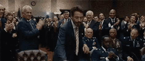 a man in a suit and tie is standing in front of a crowd of people clapping .
